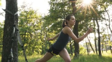 Şehir parkında Trx ile açık havada egzersiz ler yapan çekici genç kadın. Güneş ışığı, yavaş çekim