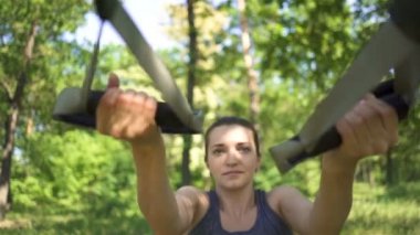 Trx spor takımı. Şehir parkında açık havada egzersiz yapan genç kadın. Yavaş çekim, yüz yakın çekim