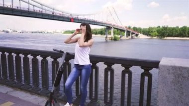 Pretty kız şehir bölgesinde elektrikli scooter yakınında durmak. Sabit atış