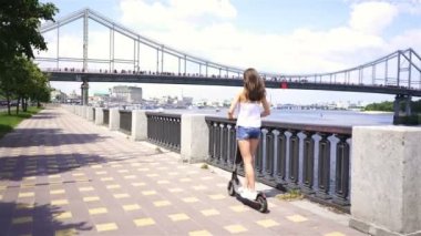 4 k. Şehir bölgesinde elektrikli scooter kullanan güzel genç bir kız. Sabit çekim, geri görünüm