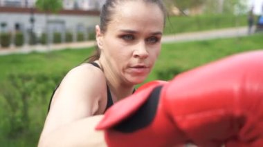 Yavaş çekim. Kırmızı eldivenli kadın boksör patlar. Şehir parkı açık, sabit çekim