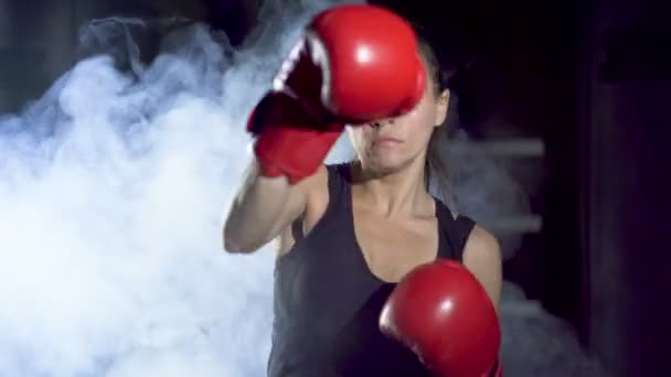 女性ボクサーは暗いトレーニングホールで 煙の中で影と戦います カメラで吹く — ストック動画