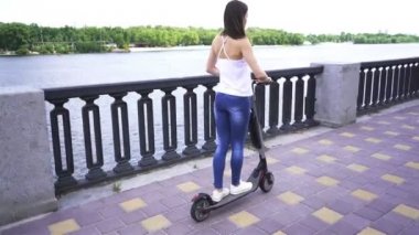 4 k. Nehir yakınındaki şehir bölgesinde elektrikli scooter kullanan kız. Sabit atış