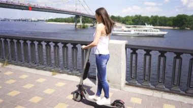 4 k. Nehir yakınındaki şehir bölgesinde elektrikli scooter kullanan güzel bir kız. Kişisel elektrikli ulaşım ekibi