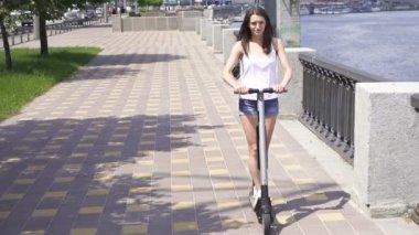 Yavaş çekim. Nehir yakınındaki şehir bölgesinde elektrikli scooter sürme Pretty kız . Sabit atış