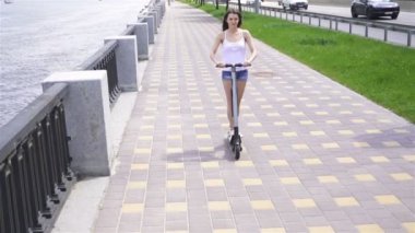 Yavaş çekim. Genç kız nehir yakınındaki şehir bölgesinde elektrikli scooter sürme . Sabit atış