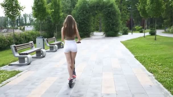 4K市立公園エリアで電動スクーターに乗って若い長い髪の女の子 安定したショット バックビュー — ストック動画