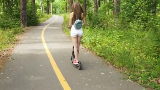 4K緑の公園エリアで電動スクーターに乗って若い長い髪の女の子 安定したショット バック — ストック動画