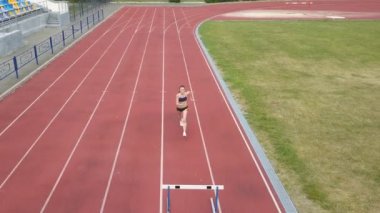 Hava. Bayan atlet pistte. Stadyum yolunda koşan genç koşucu, bariyerlerden atladı