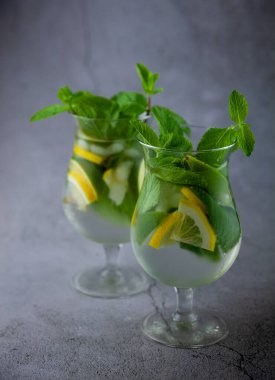Naneli limon ferahlatıcı kokteyl mojito rom ve buzlu gri arka planda cam. Koyu taş masada mojito kokteyli. İçkiler için cam gibi bir bardak. Barda limonata. Klasik içki..