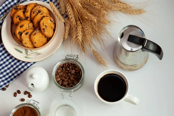 White cup of coffee and homemade round cookies with chocolate chips. Breakfast is on the table. Food at home. Still life. Coffee and coffee beans. An invigorating drink.