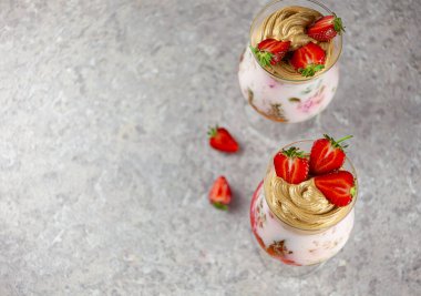 Kokteyl masanın üstünde, metin için yer var. Gri arkaplan. Soğuk yaz tatlısı üstü. Bir kase katmanlı jöle. Camın içinde tatlı jölesi olan renkli, şenlikli bir kokteyl. Çilek, yoğurt ve...