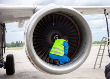 A man in a reflective vest. A male technician sits in a turbine and checks the plane's engine before flying. Aviation maintenance, repair. Airport worker clipart