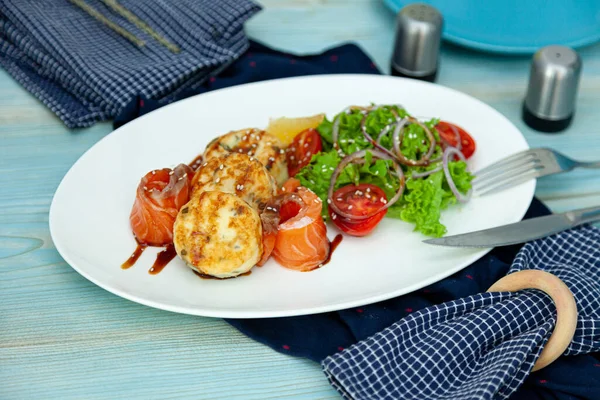 Fish cakes with salad, tomatoes and red onions in a restaurant on a white plate. Red salmon fish. Fish menu. Close-up. Healthy Omega-3 food. — Stock Image Fish Cakes Salad Tomatoes Red Onions Restaurant White Plate Red Stock Photo