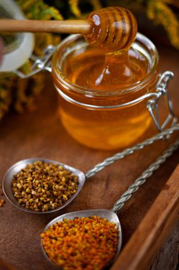 Cam kavanozda tahta kaşıkla bal. Sarı çiçekli, ahşap bir masada altın sarısı bir çubuk. Sağlıklı tatlı yiyecekler.