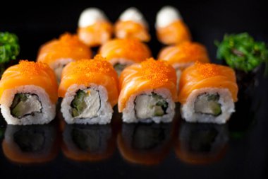 Somon suşi seti. Suşi Philadelphia 'yı kırmızı balıklı, somonlu, kırmızı havyarlı. Masaj havyarının altında yumuşak avokado ve krem peynirle yuvarlan. Siyah arka planda klasik suşi..