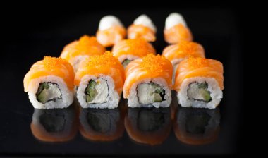 Somon suşi seti. Suşi Philadelphia 'yı kırmızı balıklı, somonlu, kırmızı havyarlı. Masaj havyarının altında yumuşak avokado ve krem peynirle yuvarlan. Siyah arka planda klasik suşi..