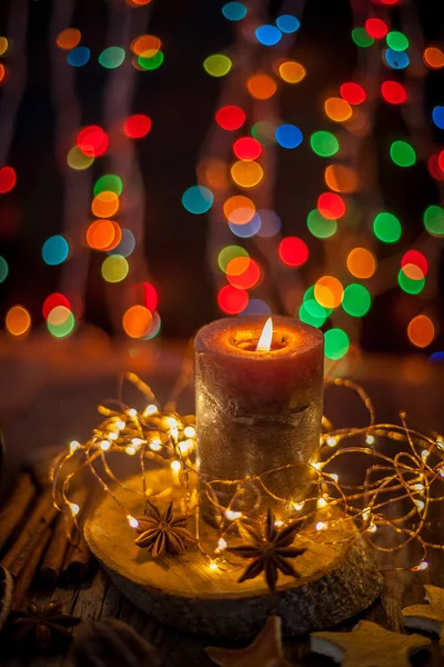 Good New Year spirit. Candle, garland, Christmas lights. Spices are anise star, an orange peel on a wooden table.