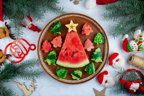 Yeni yıl yemeği. Karpuzdan yapılmış Noel ağacı. Noel dekoru masada. Şenlikli natürmort. Süslü dallar ve dekorasyonlar.