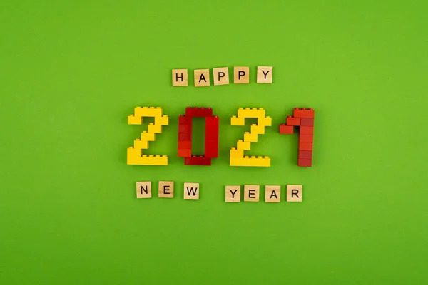 Yeni Yıl 2021 tabiri yeşil arka planda ahşap harflerle kaplıdır. İnşaatçının üst görüşünden rakamlar. Mesaj için kartpostal hazır. Flatlay. Sarı ve kırmızı sayılar. Kelimeler.