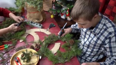 Gençler sıcak tutkal tabancasıyla çam dallarını yapıştırıyor. Noel çelengi ve ağaç için kendi ellerinle süsleme yap. Zanaat