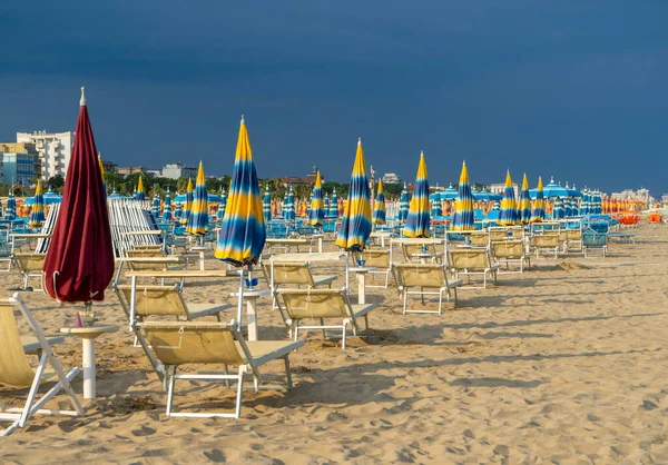 Şemsiyelerle kumlu sahilde güneşleniyorlar. Boş sahil beldesi. İtalya. Sahil şeridi şezlongunda güneş banyosu. Yazın mavi yağmurlu gökyüzü