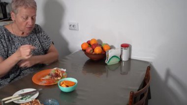 Yaşlı kadın evde salamlı pizza yiyor. Büyükannem öğle yemeğinden hoşlanıyor. Tabakta yemek var. Mangırı ye.