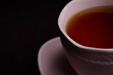 Siyah arka planda seramik çay fincanı. Siyah çay ile pembe bardak.