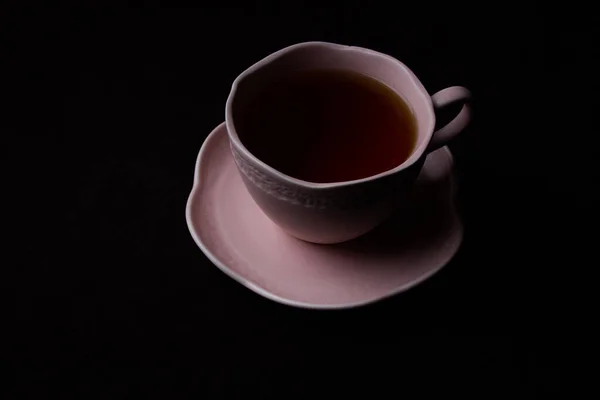Siyah arka planda seramik çay fincanı. Siyah çay ile pembe bardak.