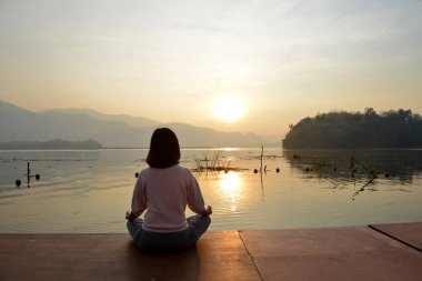 Denizin arka planında yoga yapan bir kadın ve doğan güneşin ışığında altın gökyüzü..