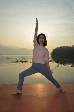Denizin arka planında yoga yapan bir kadın ve doğan güneşin ışığında altın gökyüzü..
