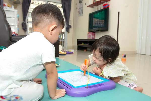 little girl and little boy playing with magnetic drawing board on the floor