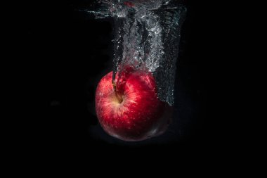 Siyah arkaplanda izole bir şekilde suya düşen elma.