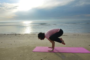 sağlıklı bir kadın gün doğumunda plajda yoga yapıyor.