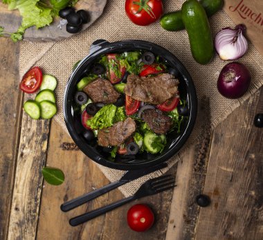 Yeşil salata, domates ve zeytin ile ızgara sığır biftek dilimleri.