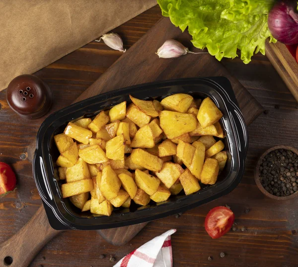 Gebakken aardappelen met kruiden afhaalmaaltijden in zwarte container. — Stockfoto