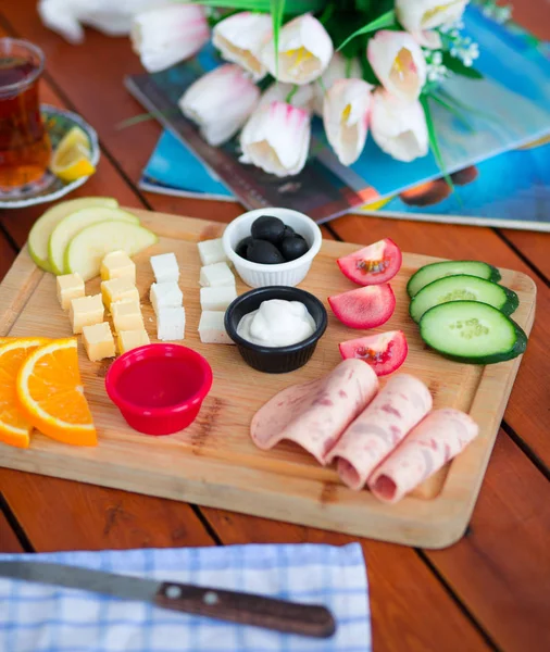 Breakfast platter with salami, olives, cream cheese, cheese, tomato, cucumber, jam and glass of tea.