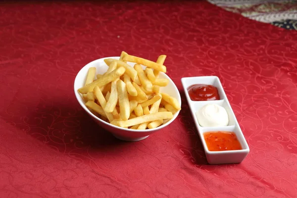 French fries in white bowl served with mayonnaise, ketchup and hot chili sauce. — Stock Photo, Image