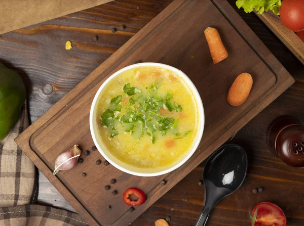 Chicken broth vegetable soup in disposable cup bowl served with green vegetables.