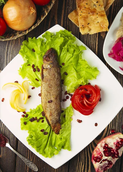 Grilled silver fish served with lemon, lettuce, tomato and pomegranate seeds.