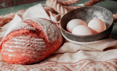 Etrafında yumurta kase ile üstüne unlar ile beyaz bir havlu üzerinde ev yapımı ekmek.