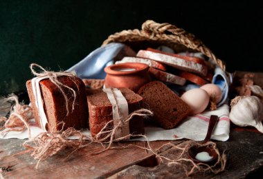 Beyaz bir havlu üzerinde süt, yumurta ve sarımsak bir tencere ile beyaz kağıt ve tustik iplik ile sarılmış siyah ekmek dilimleri.