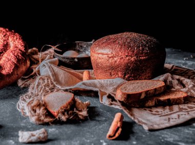 Üzerinde otlar ile bütün bir geleneksel yuvarlak siyah ekmek yan görünümü, bir mutfak taşı üzerinde rustik bir havlu üzerinde ince dilimler.