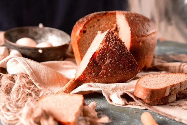 Vista lateral pan de trigo y rebanada grande en una toalla blanca con hilo rústico y tazón de huevo alrededor de una mesa de piedra . —  Fotos de Stock