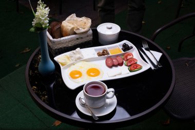 Kahvaltı tabağı, kızarmış yumurta, ekmek dilimleri ve siyah masada bir fincan çay.