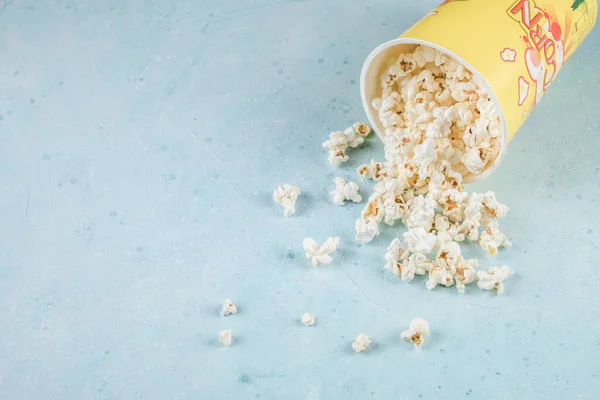 Popcorns espalhados para fora de uma caixa de recipiente amarelo na mesa azul — Fotografia de Stock