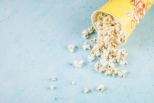 Popcorns fora de uma caixa de recipiente amarelo na mesa azul — Fotografia de Stock