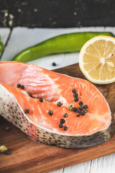 Rodajas de salmón con bolas de pimienta negra y limón en una tabla de madera — Foto de Stock