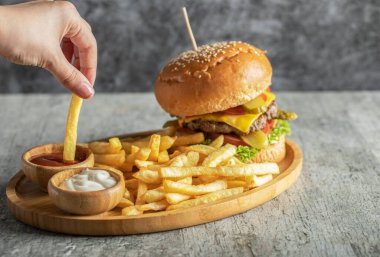 Ahşap bir tabakta soslu hamburger ve kızarmış patates.