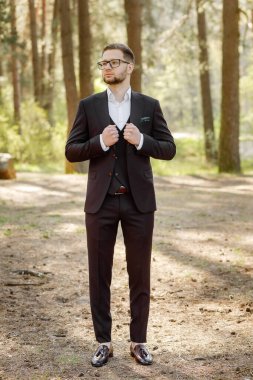 Siyah takım elbiseli bir adam ormanda poz veriyor..